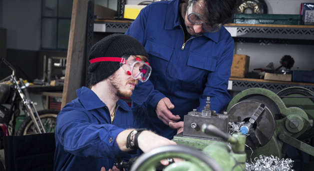 Young mechanic apprentice in wheelchair working on turning lathe